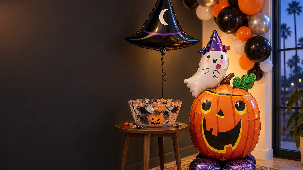 Halloween party corner with a pumpkin-and-ghost balloon, witch hat balloon, orange, black and silver balloon garland and a candy bowl